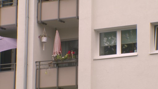 Das Fenster einer Wohnung mit angrenzendem Balkon, auf dem ein roter Sonnenschirm steht